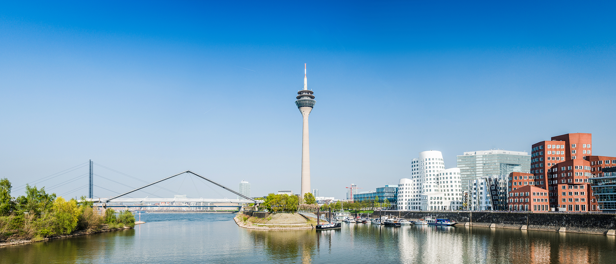 Ein Aufnahme des Rheinufers mitten in Düsseldorf zeigt in der Ferne den Rheinturm und die Rheinkniebrücke.